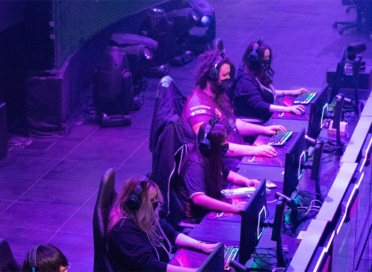 Four Esports members shown in the foreground with a purplish lighting illuminating them and their computers