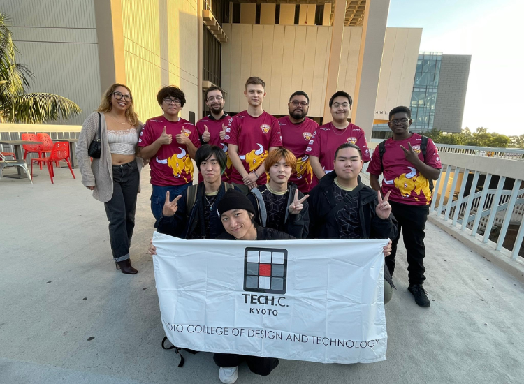 A group of students posing in front of the Library. One student is crouched and holding up a banner that reads "Tech.C. Kyoto - college of design and technology